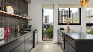Una cocina moderna con armarios oscuros, encimera de acero inoxidable, horno integrado y ventana con vistas a la ciudad.