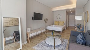Un salon moderne et bien éclairé, avec un canapé, une table basse, un téléviseur et un lit doté d’une table de chevet.