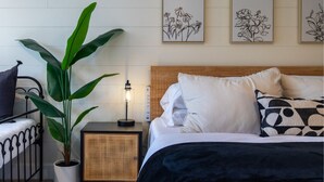 Un dormitorio ordenado con cama, mesita de noche, lámpara, planta en maceta y decoración en la pared.