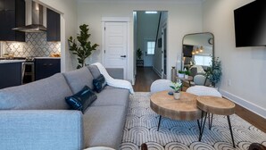 Una sala de estar moderna con un sofá gris, una mesa de centro y un comedor con cocina al fondo.