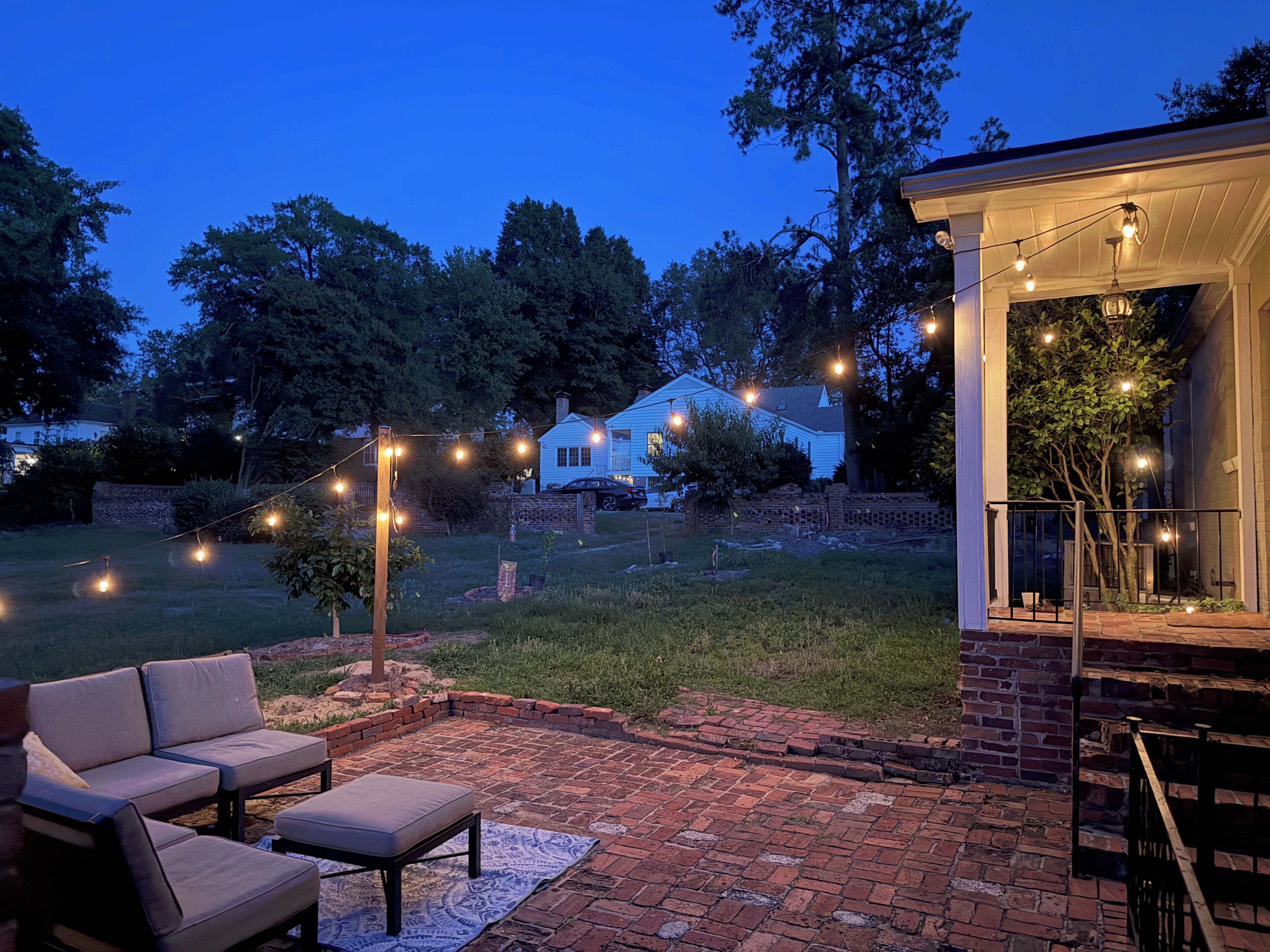 An outdoor patio area with brick flooring, a seating arrangement, and string lights.