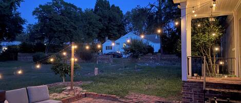 An outdoor patio area with brick flooring, a seating arrangement, and string lights.