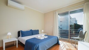 Hotellihuone, jossa on sänky, kaksi yöpöytää, tuoli, parveke, jolta on näkymä, ja ilmastointilaite.