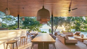 Un área de comedor al aire libre con una mesa de madera larga, varias sillas y un ventilador de techo.