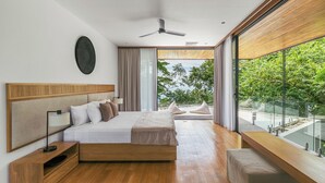 Un dormitorio moderno con una cama grande, mesitas de noche, un ventilador de techo y vistas a un balcón con barandilla de vidrio.
