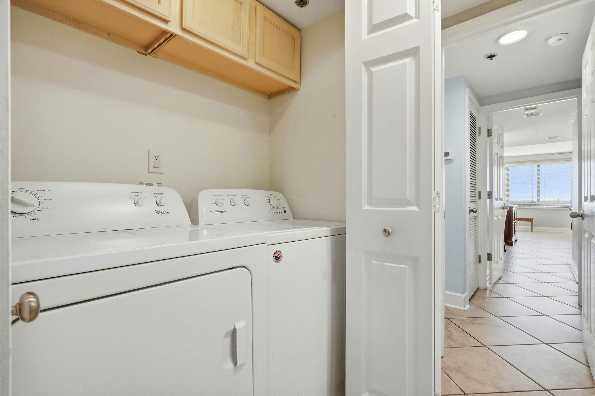 Un cuarto de lavandería con lavadora y secadora, armarios de madera y piso de baldosas.