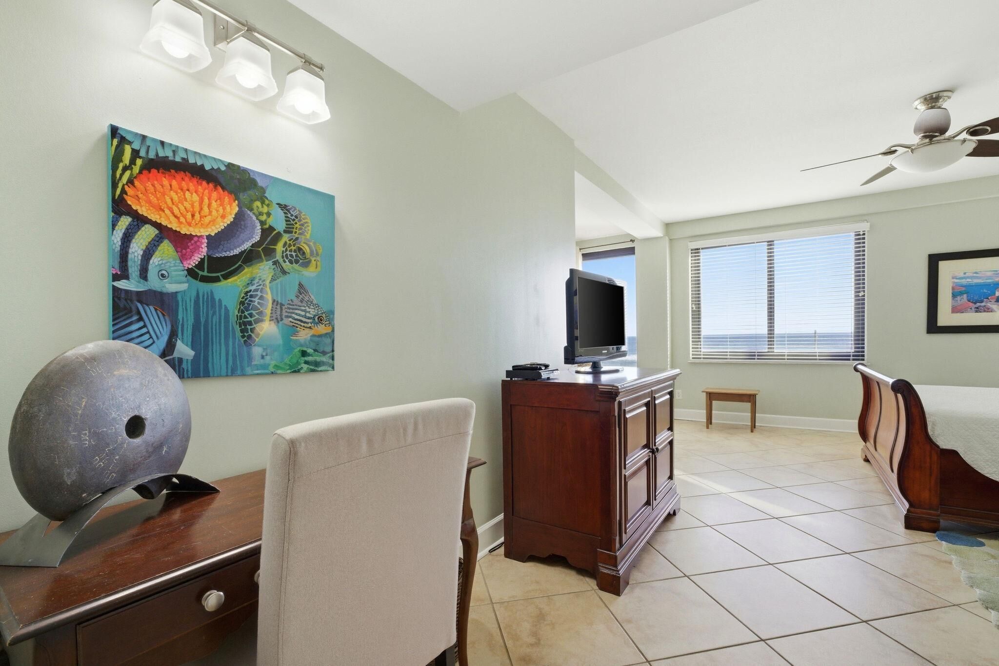 A bedroom with a bed, a desk with a computer, a chair, a television, and a painting on the wall.