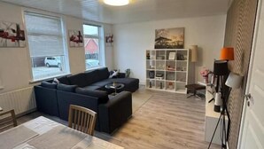 A spacious living area with a sofa set, a dining table, and a bookshelf.