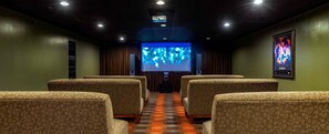 Ein Theater mit gemusterten Sitzplätzen, einer großen Leinwand und einem Projektor.