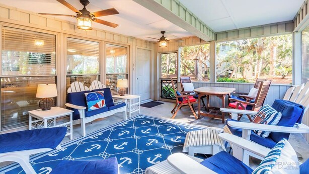 Un espace extérieur aménagé avec des meubles blancs, des coussins bleus et un tapis aux motifs marins, le tout abrité.