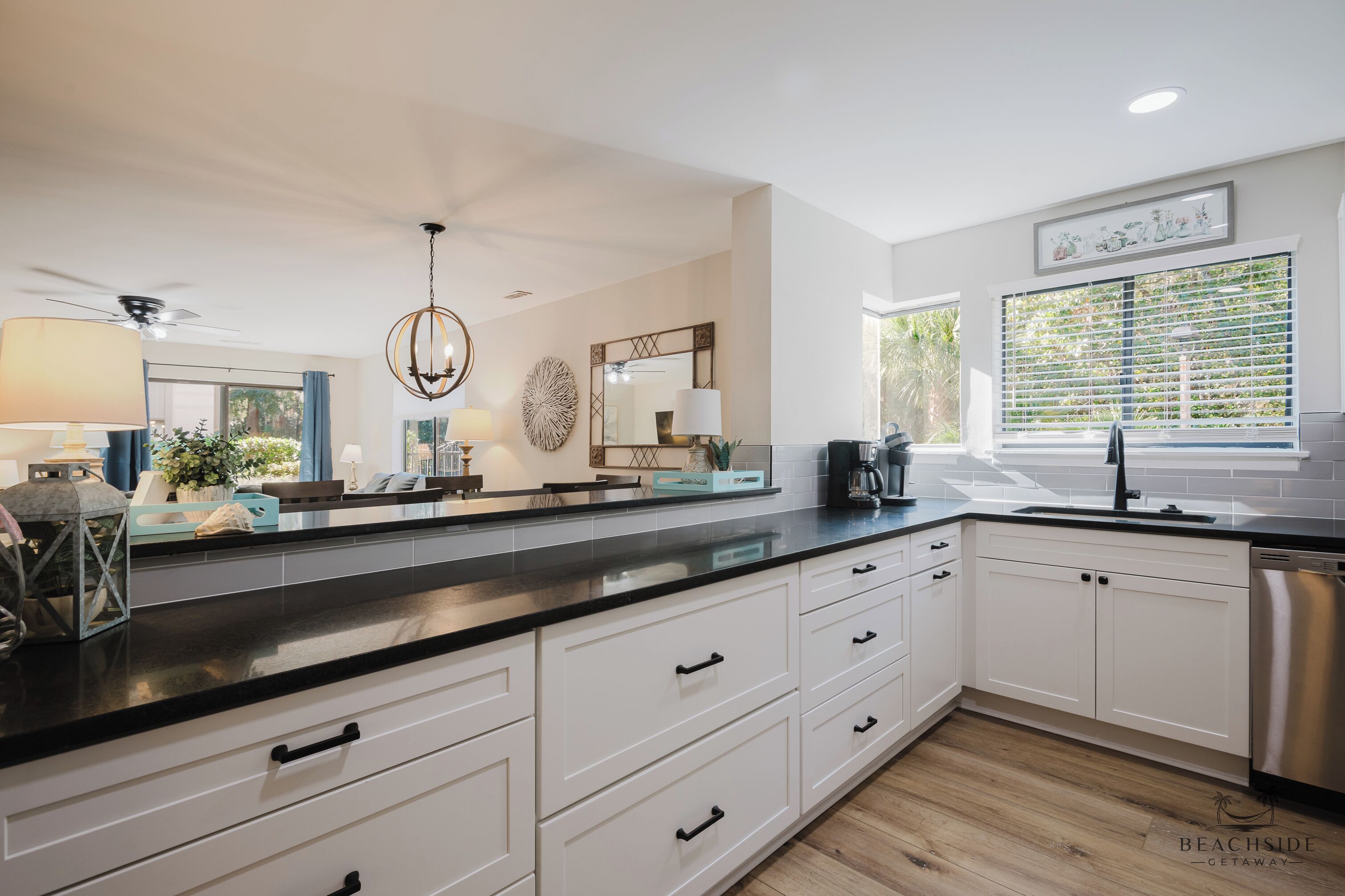 A modern kitchen with white cabinetry, black countertops, and a stainless steel dishwasher.