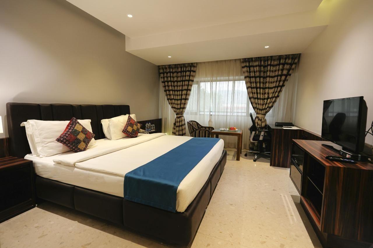 A hotel room with a large bed, a desk, a chair, and a TV.