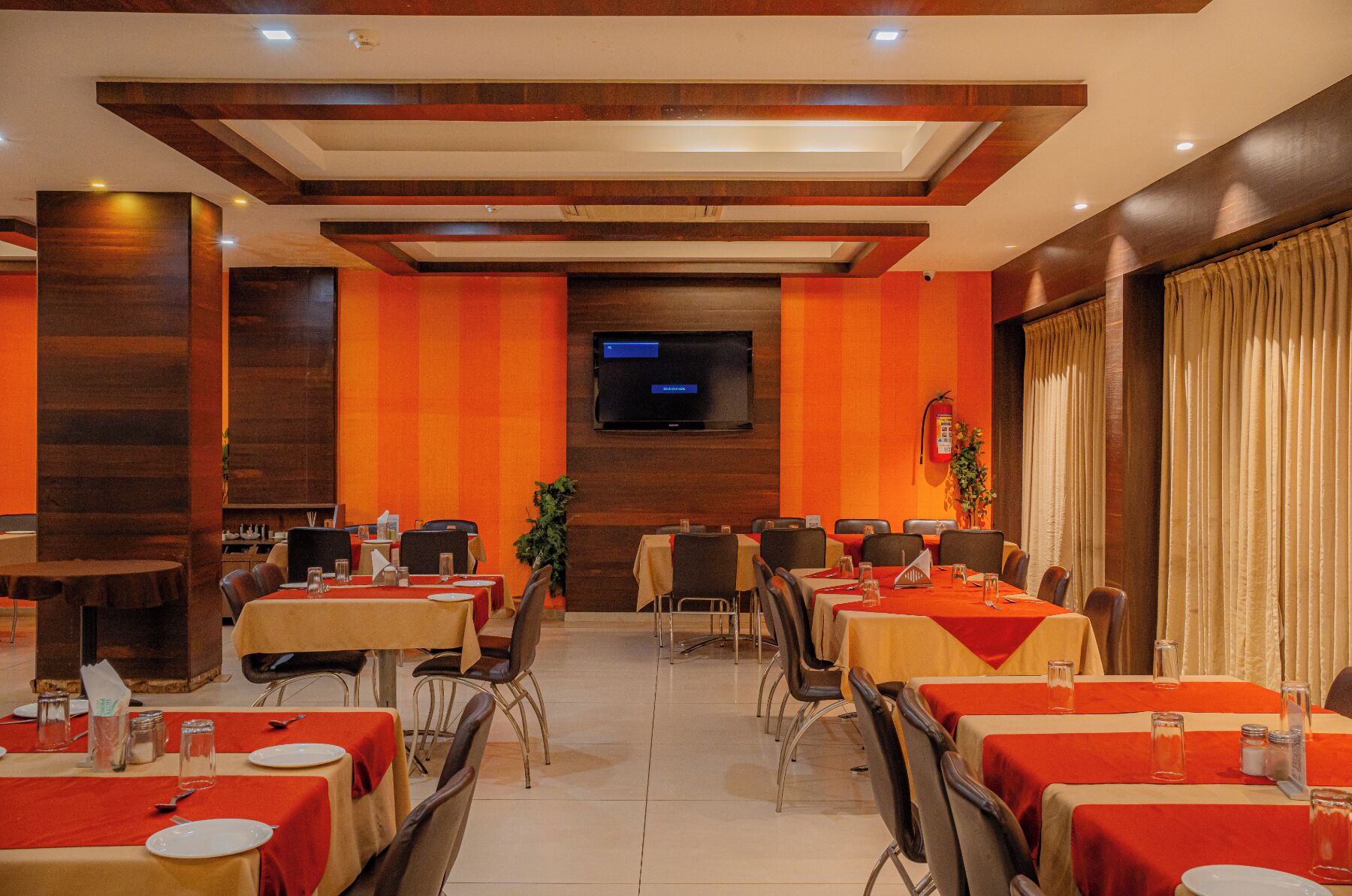 A conference room with tables set for meetings, a flat-screen TV on the wall, and a fire extinguisher.