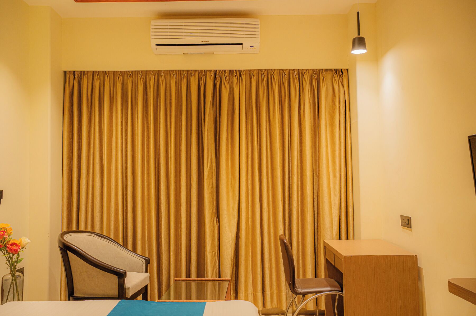 Een hotelkamer met een bed, twee stoelen, een bureau, een wandairconditioner en een hanglamp.