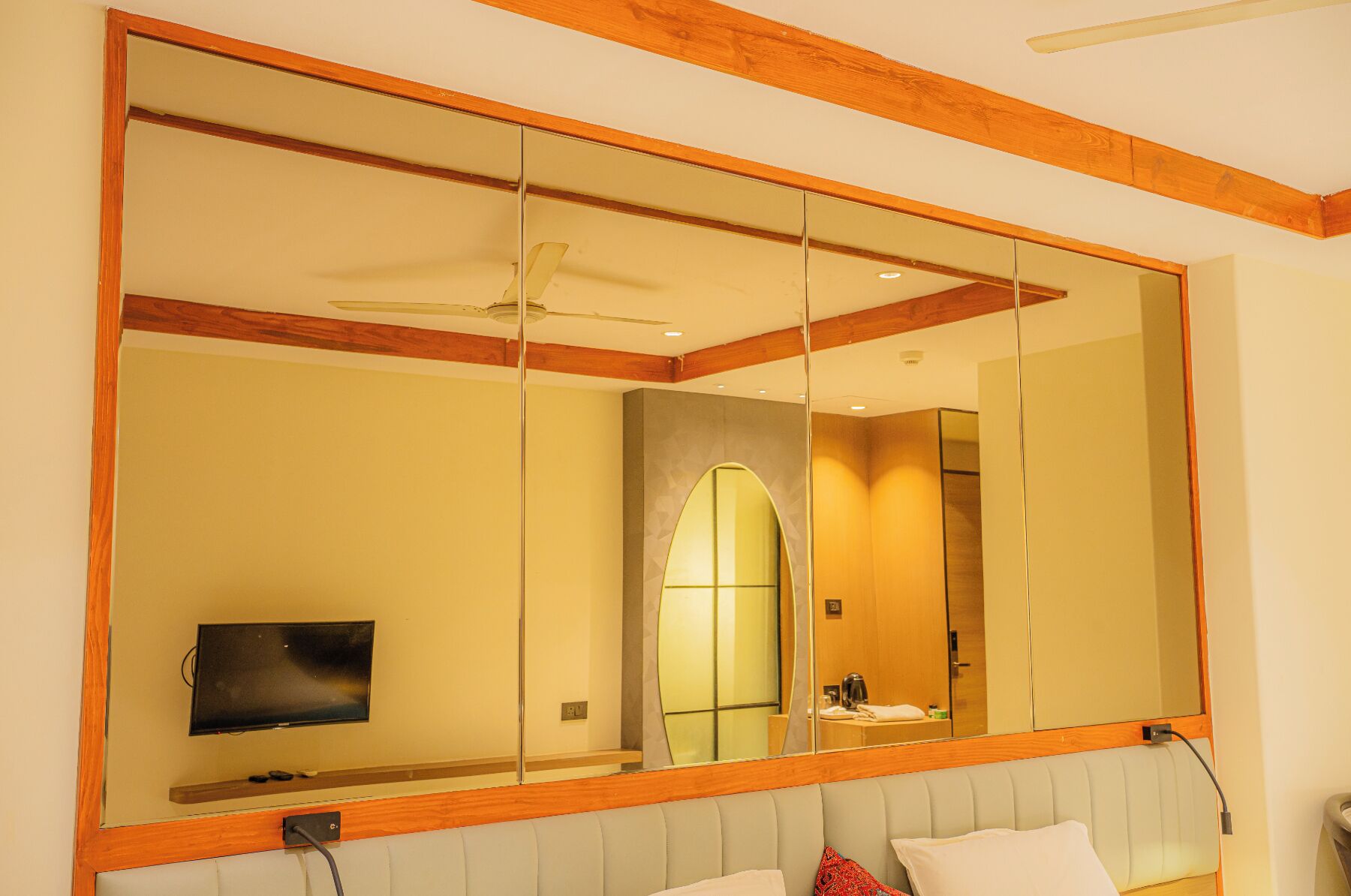 Una habitación de hotel con un espejo grande, un televisor y una cama con almohadas.