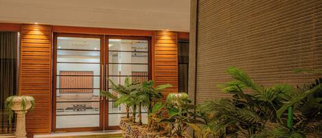 A modern lobby with a wooden floor, a glass door entrance, and a row of potted plants.