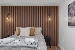 Ein Schlafzimmer mit einer Wand aus Holzlatten, einem Bett mit aufgerollten Handtüchern, zwei Wandleuchten und einem Bild an der Wand.