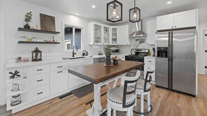 A modern kitchen with white cabinetry, a central island with bar stools, a stainless steel refrigerator, and pendant lighting. - 3 bed,2 bath Luxury & Private Turf Yard (Rapid City)