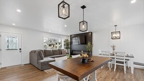 A modern living room with a sofa, a dining table, and a TV. - 3 bed,2 bath Luxury & Private Turf Yard (Rapid City)