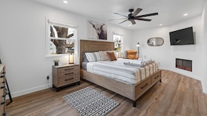 A bedroom with a bed, bedside tables, a ceiling fan, a fireplace, and a TV. - 3 bed,2 bath Luxury & Private Turf Yard (Rapid City)