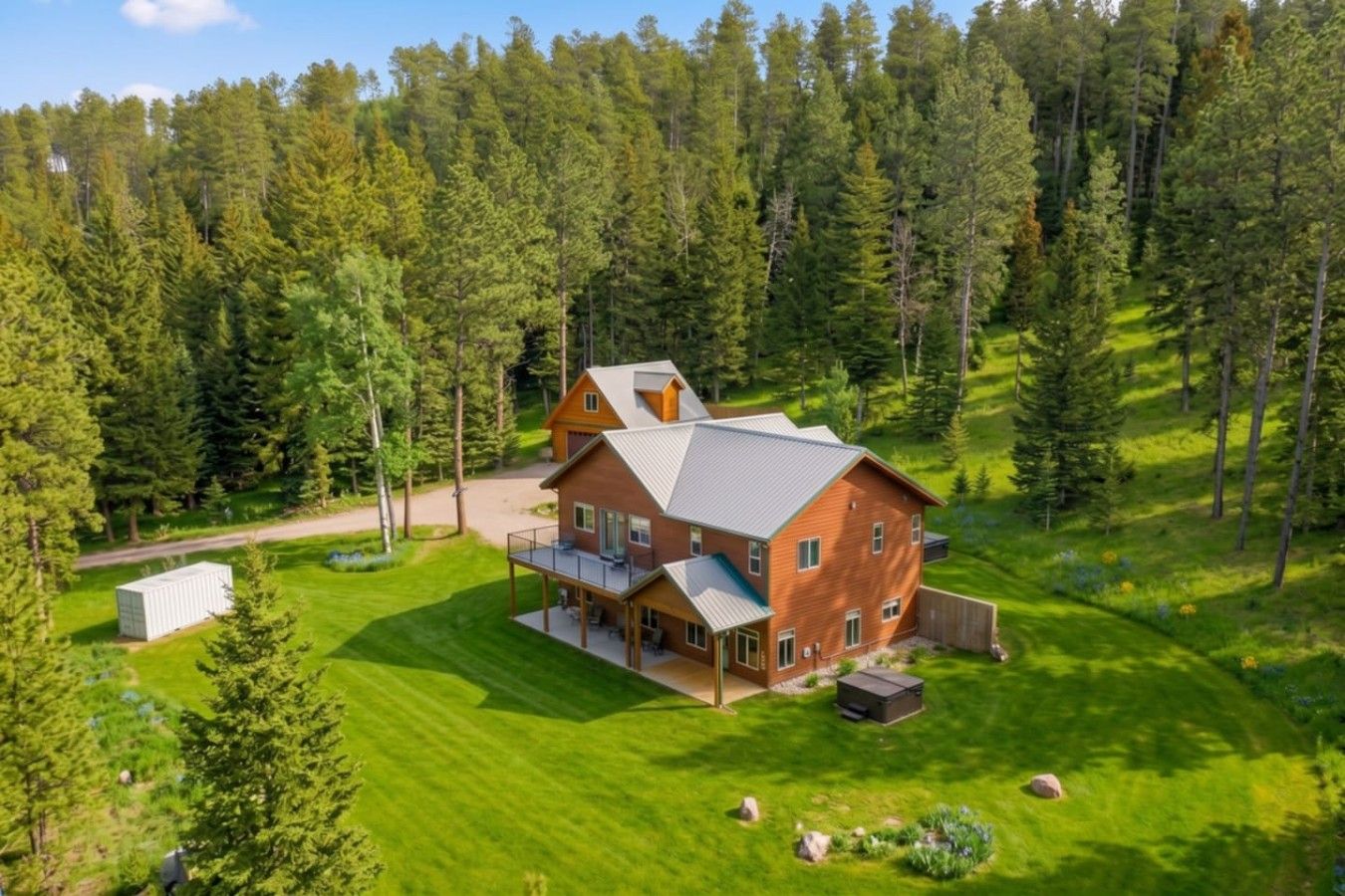 A large, two-story wooden cabin with a spacious deck, surrounded by a dense forest.