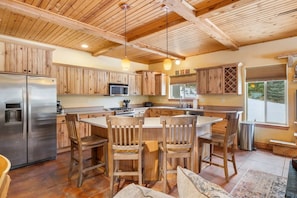 A kitchen with wooden cabinets, a stainless steel refrigerator, a central island with chairs, and a large window.