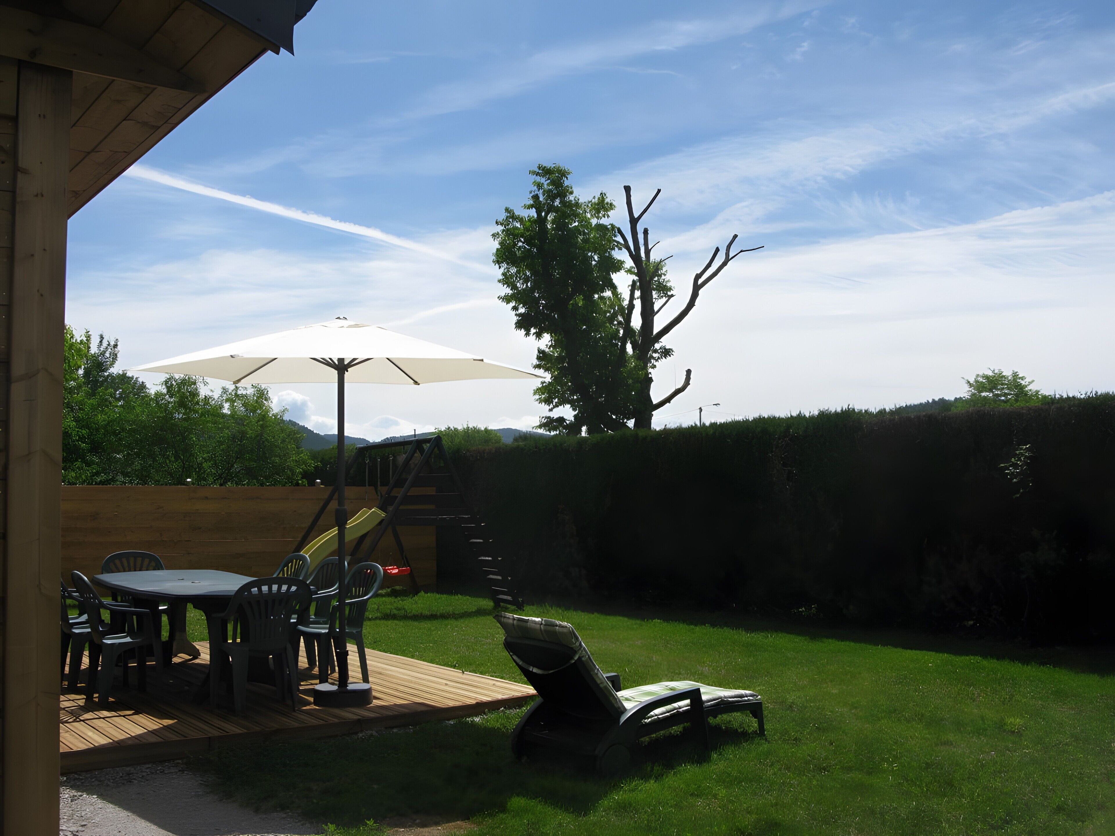Une terrasse avec une table et des chaises, un toboggan et un parasol.