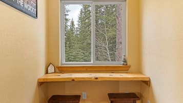 Quarto de canto com janela para uma floresta, um banco de madeira e uma mesa pequena.