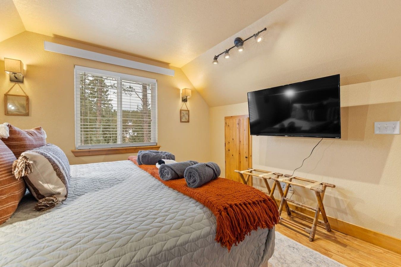 Ein Schlafzimmer mit einem Bett, einem an der Wand montierten Fernseher, einem Fenster mit Jalousien und einer Holztür.