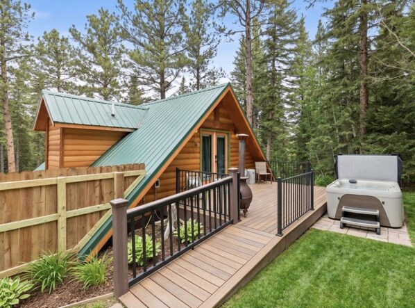 A wooden cabin with a deck, a hot tub, and a fenced yard.