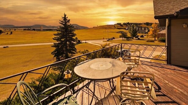 Una terraza con mesa y sillas, con vistas a un campo y colinas lejanas.