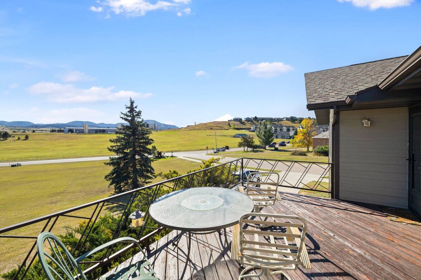 A deck with a table and chairs, overlooking a grassy field and distant buildings.