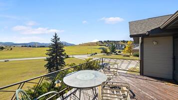 A deck with a table and chairs, overlooking a grassy field and distant buildings.