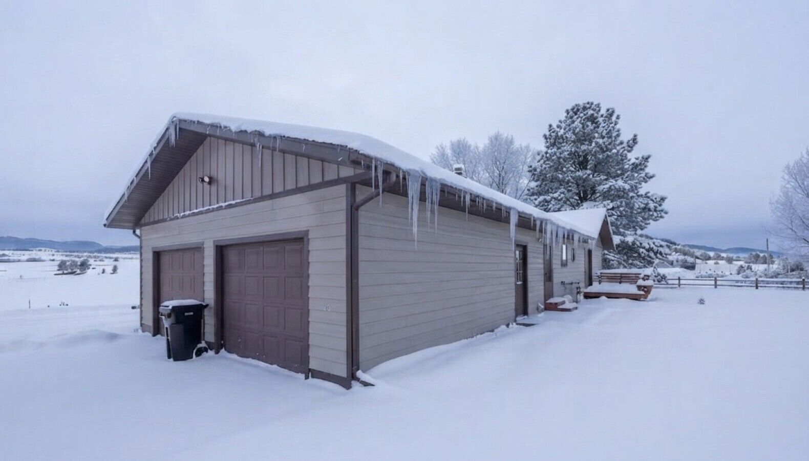 A single-story building with a garage door, a covered porch area, and a snow-covered landscape.