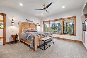 Ein Schlafzimmer mit einem großen Bett, einer Bank, einem Deckenventilator und einem Fenster mit Blick auf Bäume.