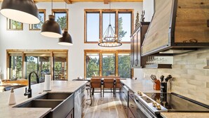 A modern kitchen with large windows, a central island, and a dining area.