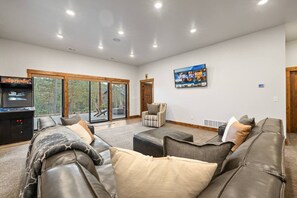 A spacious living room with a large leather sofa, a television mounted on the wall, and a gaming console. - Sleeps 14, Hot tub, OutdoorFireTable, HeatedGarage (Lead)