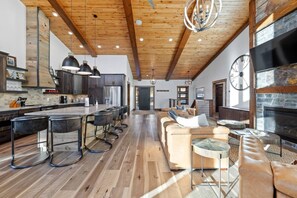 A spacious living area with a large sofa, a fireplace, and a kitchen with modern appliances. - Sleeps 14, Hot tub, OutdoorFireTable, HeatedGarage (Lead)