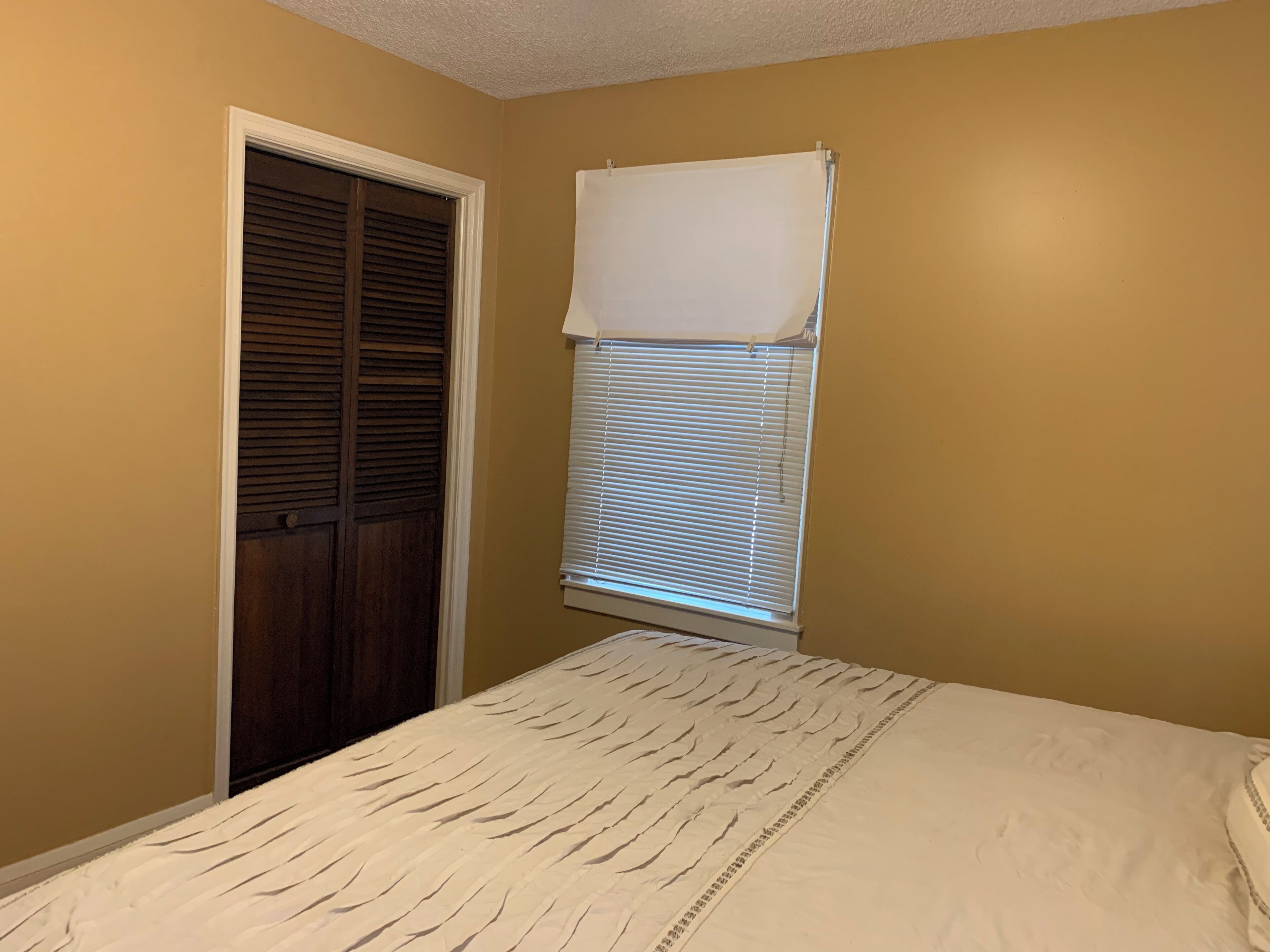 Een slaapkamer met een bed, een kast en een raam met jaloezieën.