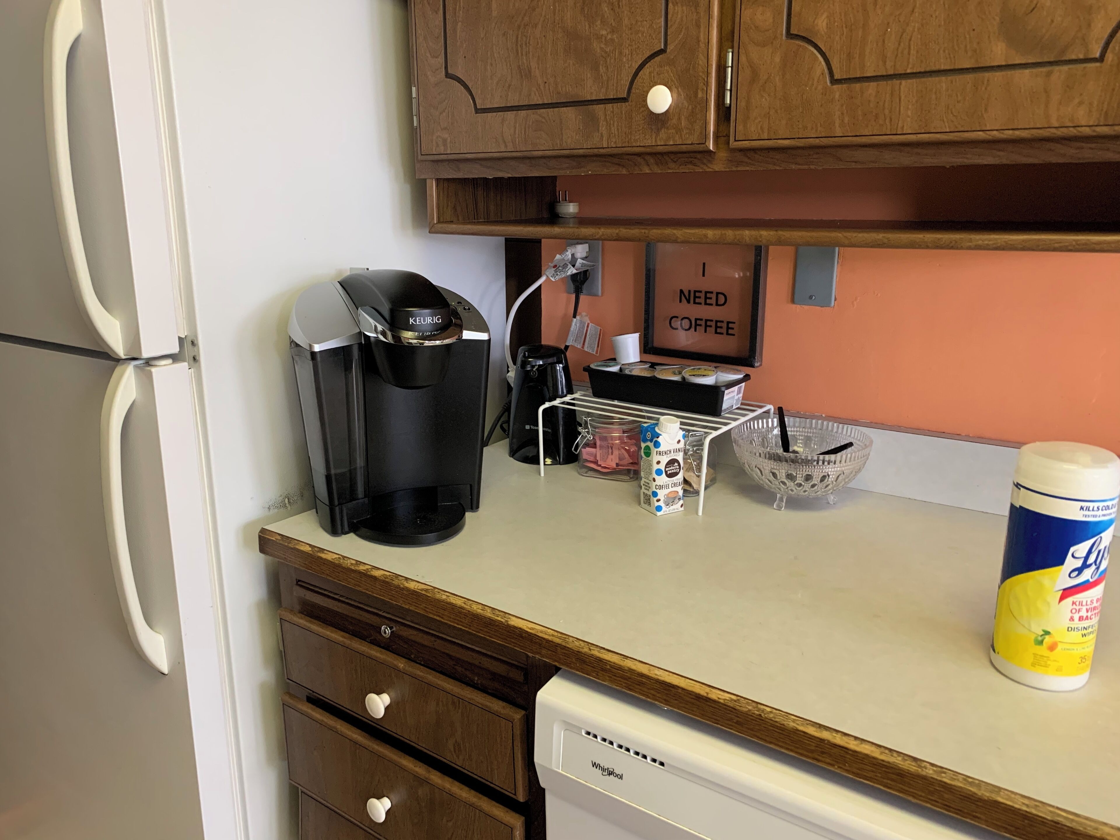 A kitchen with a coffee maker, a milk jug, a coffee creamer, and a dish rack.