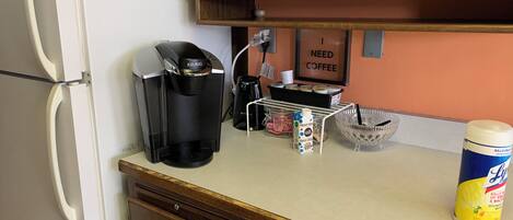 A kitchen with a coffee maker, a milk jug, a coffee creamer, and a dish rack.
