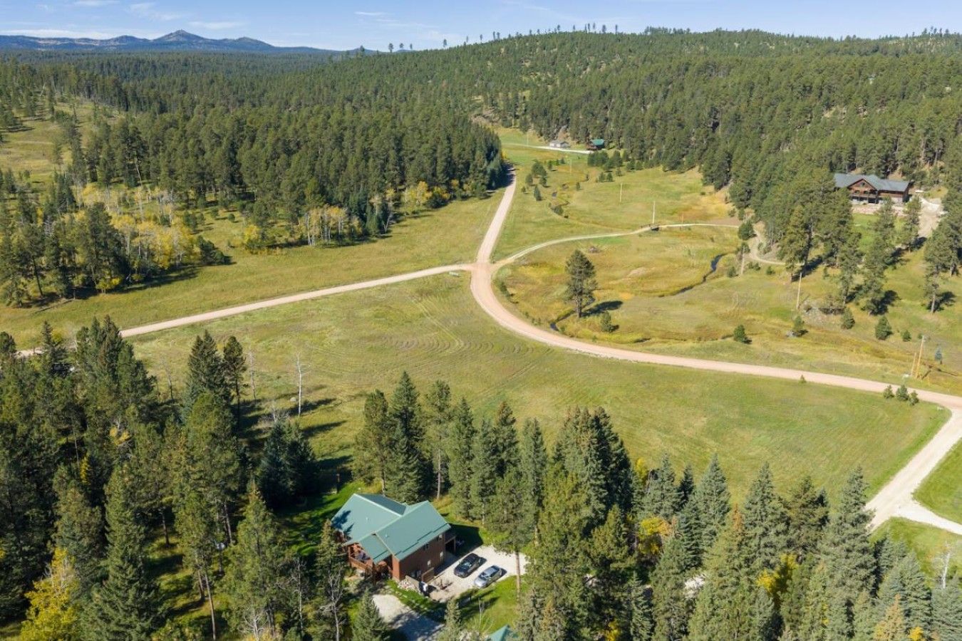 Eine abgelegene Holzhütte, umgeben von dichtem Wald, mit einer unbefestigten Straße davor.