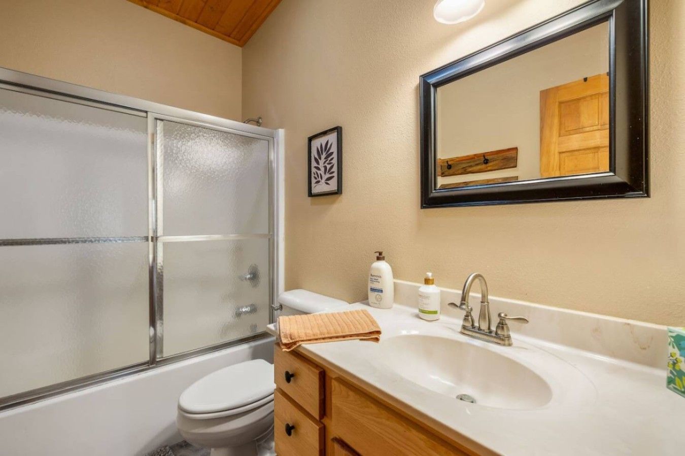A bathroom with a glass shower enclosure, a white sink with a mirror above it, and a toilet.