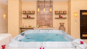 Et spa-rum med jacuzzi, hylder med stearinlys og en stenvæg.