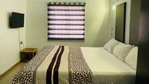 A bedroom with a bed, a television, a window with blinds, and an air conditioning unit. - Mabala Millennium  Hotel (Abuja)