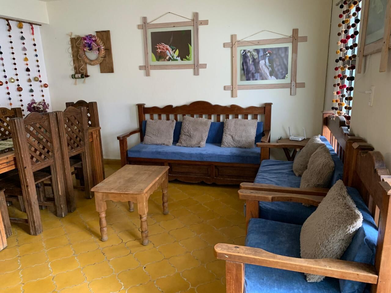 A cozy living room with a wooden sofa, matching chairs, a wooden coffee table, and a yellow-tiled floor.