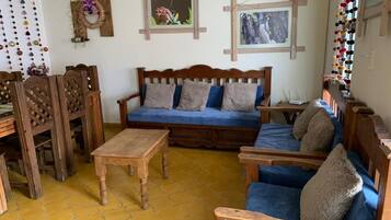A cozy living room with a wooden sofa, matching chairs, a wooden coffee table, and a yellow-tiled floor.