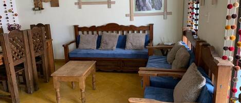 Una sala de estar acogedora con un sofá de madera, sillones azules y una mesa de centro de madera.