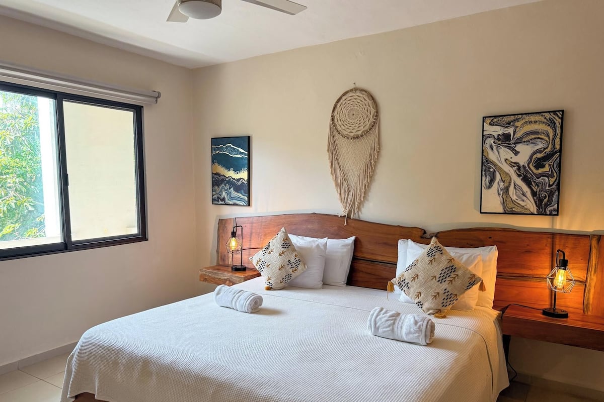 A neatly made bed with white linens, a wooden headboard, and two bedside tables with lamps.