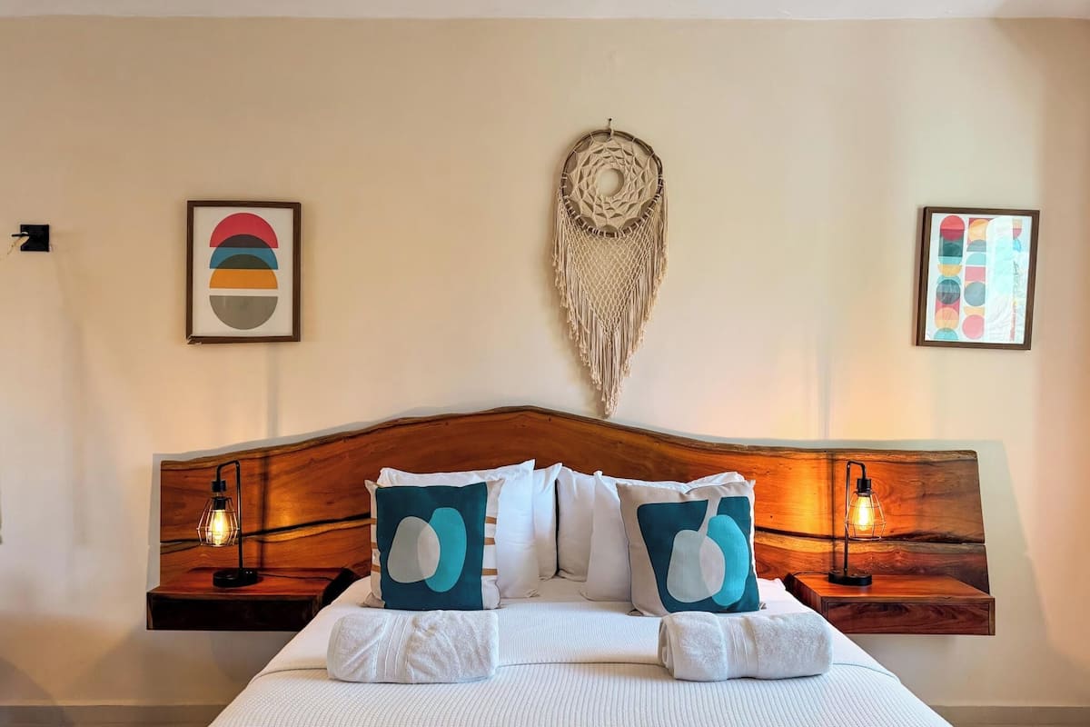 A neatly made bed with white bedding and teal pillows, a wooden headboard, and two bedside tables with lamps.